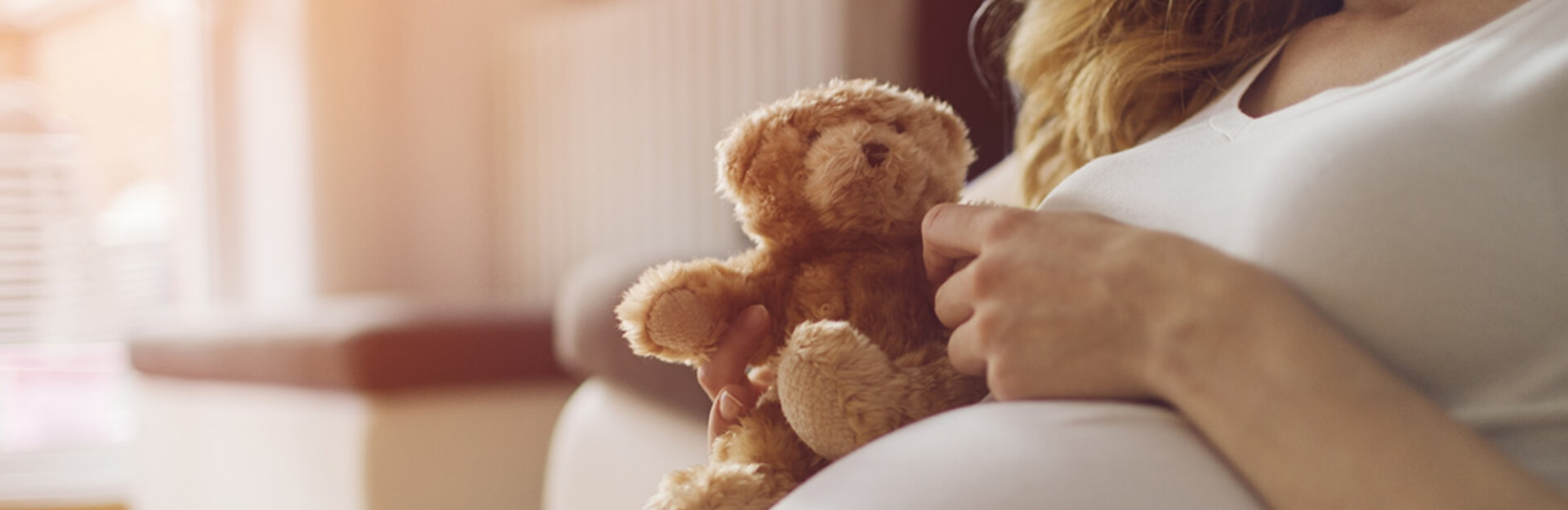 Una mamma in cinta che coccola un peluche che sta pensando alle assicurazioni per lei e per la sua famiglia 