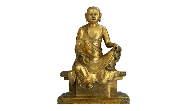 Statua in bronzo dorato raffigurante l'ArhatKalika, La figura è riconoscibile dalla coppia di orecchini di grandi dimensioni sorretti nelle mani, a lui donati da esseri celesti semidivini.